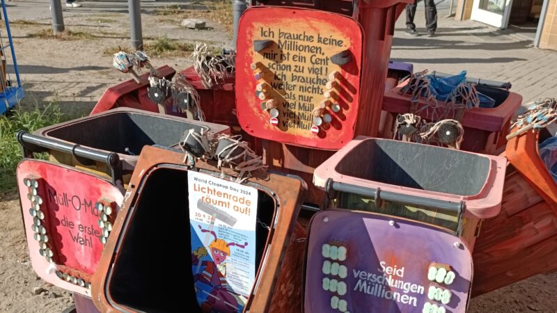 Das Bild zeigt bunt gestaltete Mülltonnen in einer Nahaufnahme. Ein Flyer des Clean Up Day 2024 wurde in einen der offenen Deckel geklebt.